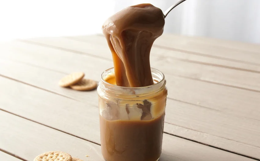 Un frasco de manjar blanco con una cuchara y galletas